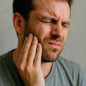 Hombre joven con dolor mandibular tocándose la cara debido al bruxismo.